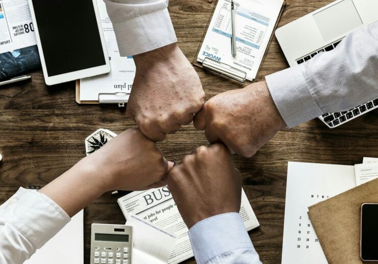 Four colleagues fist bumping over a desk to celebrate a new hire